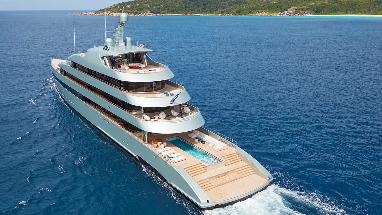 A luxurious superyacht for sale features a private pool while cruising through crystal-clear blue waters.
