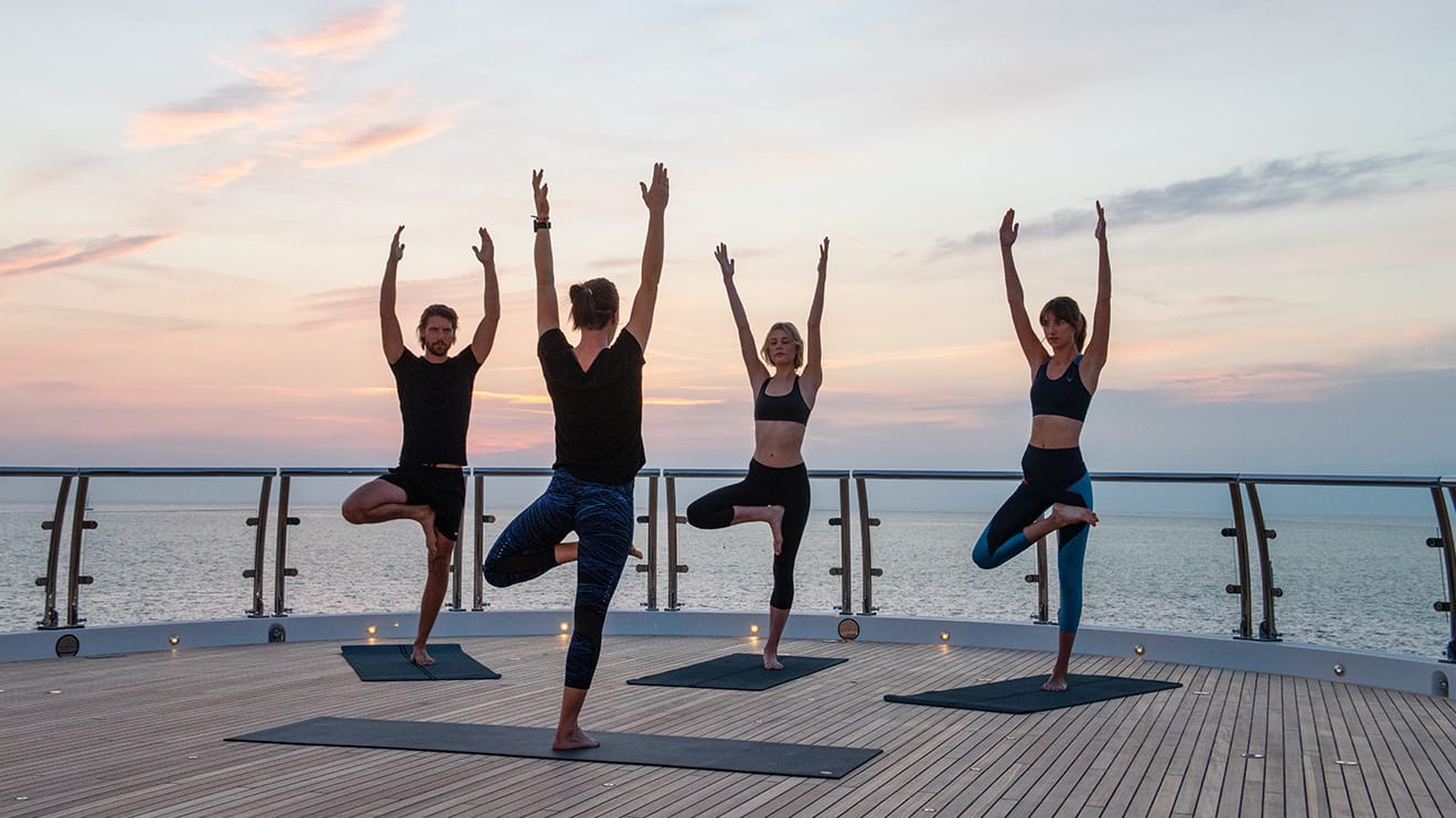 Group practicing yoga on deck at sunset, experience a luxury yacht charter lifestyle.