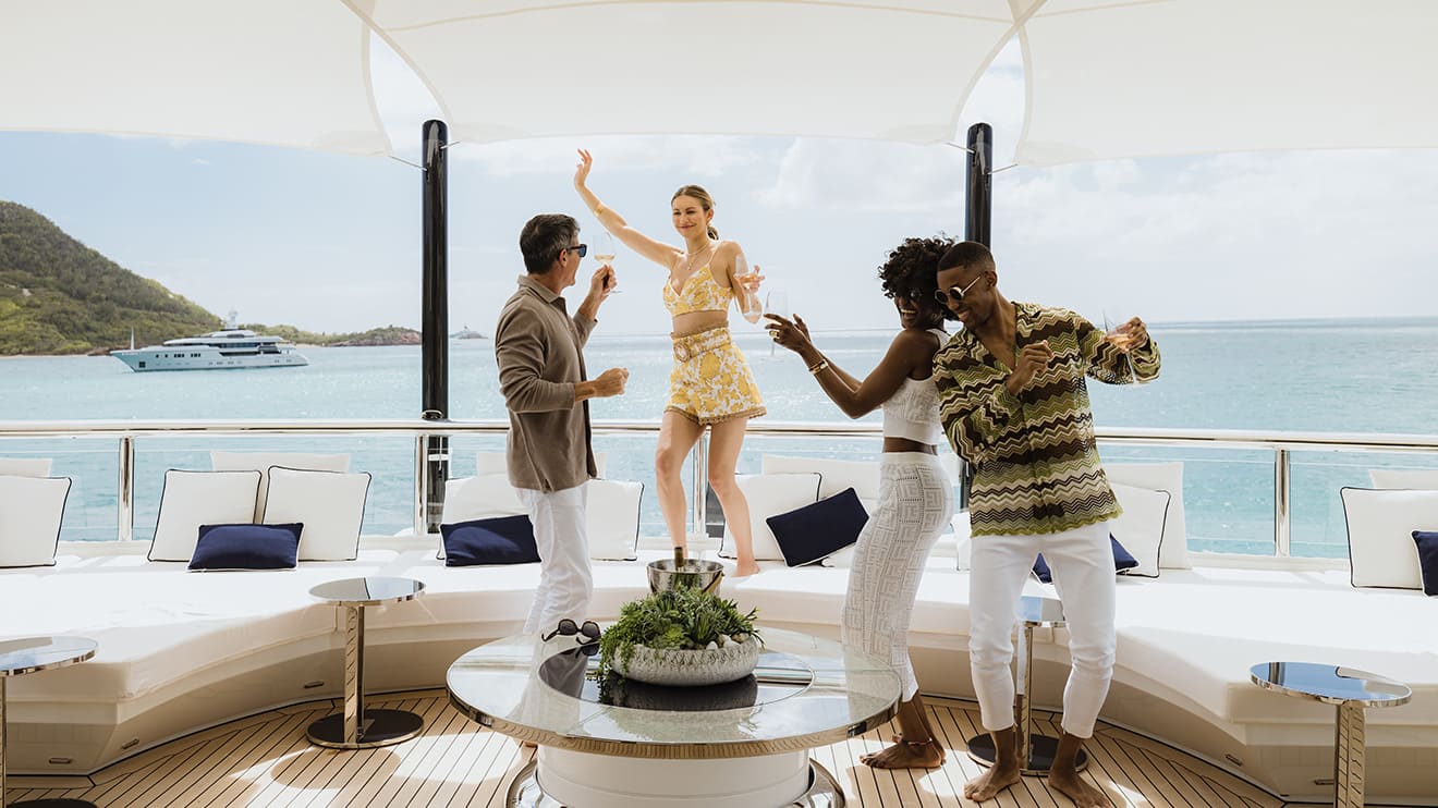 A group enjoys a lively party on a luxury yacht charter deck, with a stunning ocean view in the background.