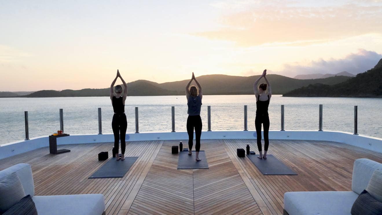 Group practicing yoga on deck at sunset, experience a luxury yacht charter lifestyle.