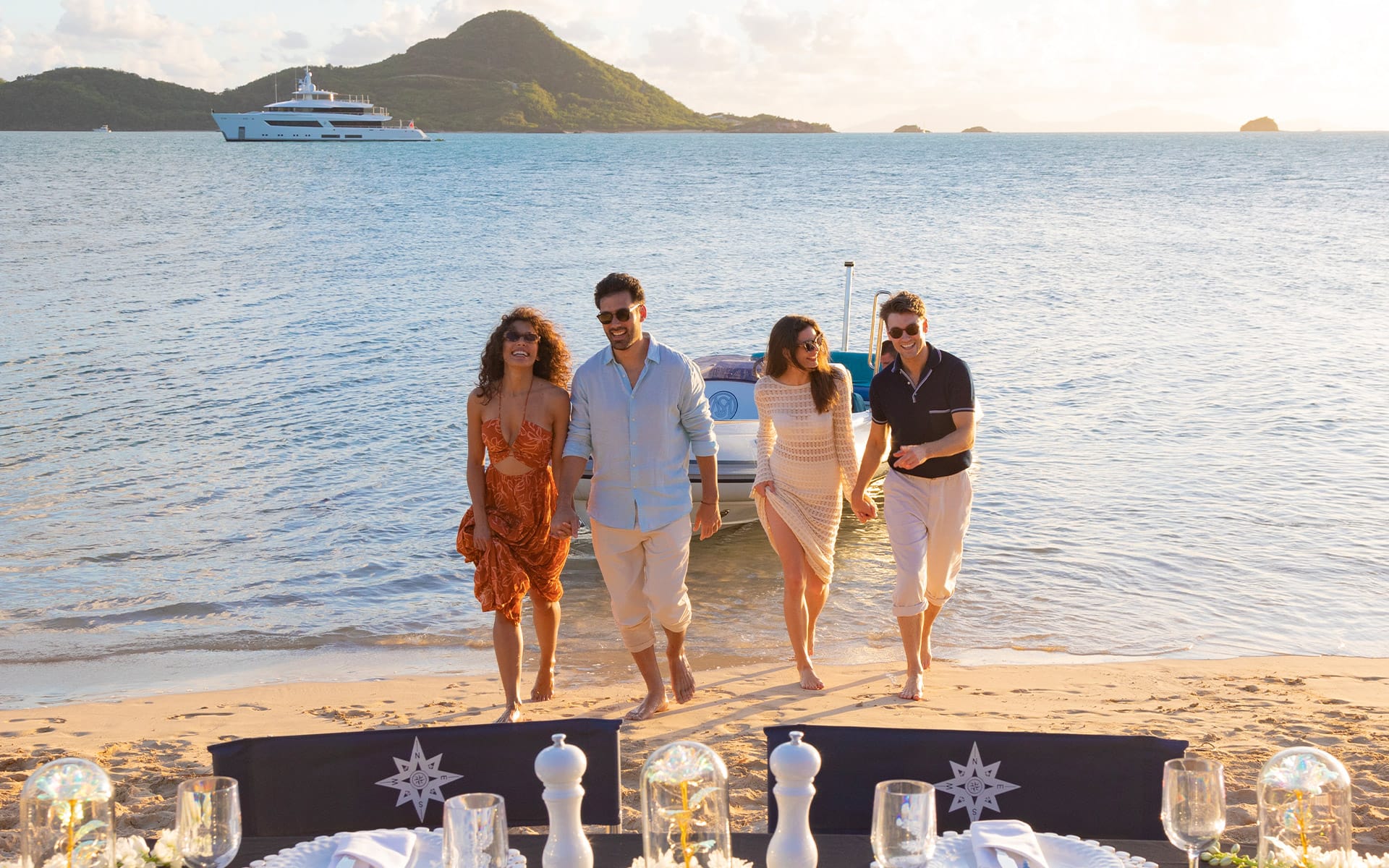 Charter guests arriving to a beach setup with charter yacht in the background