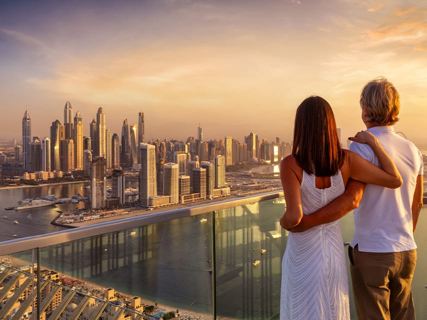 A couple surveys the cityscape at sunset. As they get ready to buy yacht, Dubai Boat Show will be the perfect place to shop.