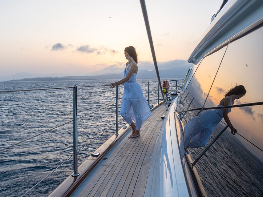 A woman relaxes on the deck of her luxury superyacht charter, St Barths sun setting over the islands in the distance.