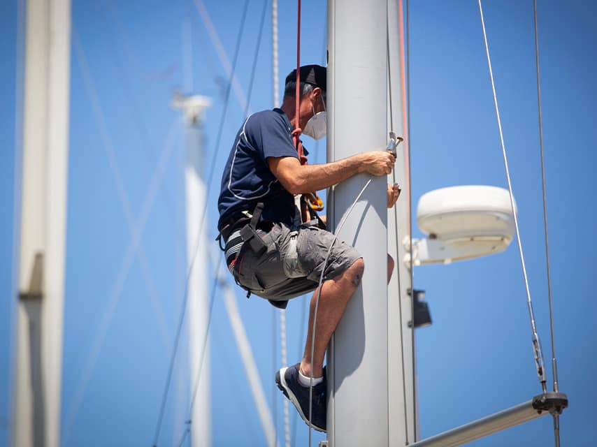 A technician climbs the mast of a sailing yacht, ensuring nothing is missed in the high standards of luxury yacht maintenance with Edmiston.