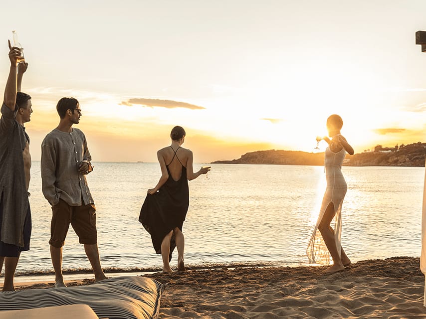 A group of friends enjoys cocktails by the sea at Astir Beach, Athens during their private yacht charter in Greece.