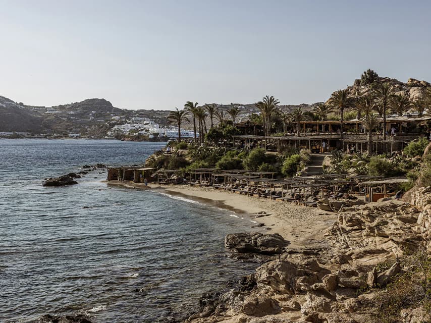 Experience the bohemian elegance of sunset rituals at the private beach of Scorpios Mykonos from a luxury yacht charter in the Greek Islands.