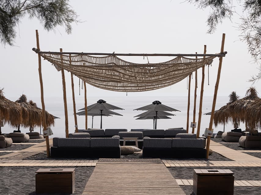 A chic beachside lounger at Wet Stories, Santorini, offers a beachfront view, the ultimate destination for a mega yacht charter in Greece.