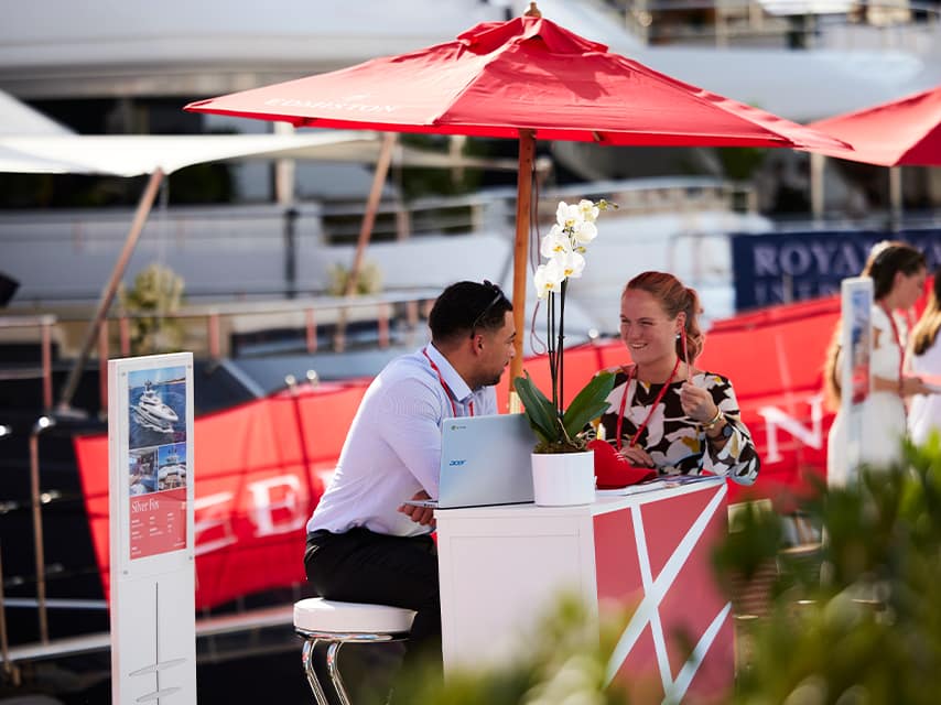An Edmiston staff member greets a visitor at the Edmiston Stand of the Monaco Yacht Festival, offering VIP service to yacht buyers and charterers.
