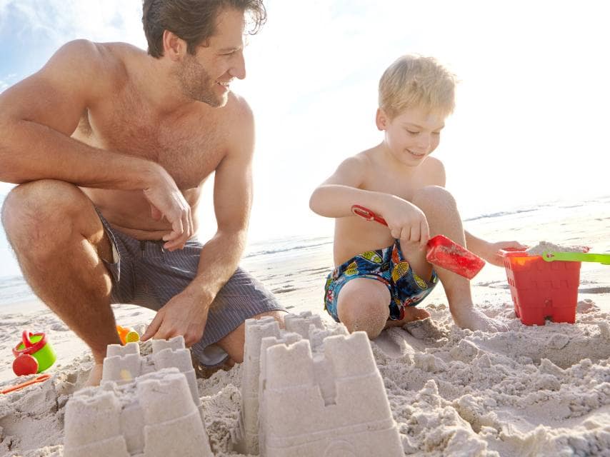 Father and son build a sandcastle during a family adventure on a sandy Greek beach during a family Med yacht charter.