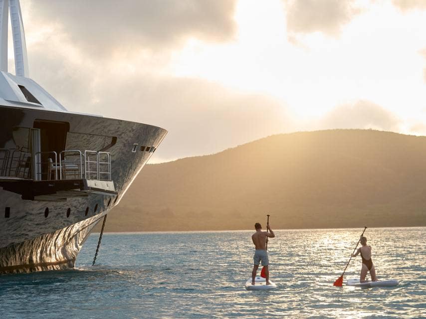 Couple paddleboarding at sunset near ARBEMA 72 during a yacht watersports experience.