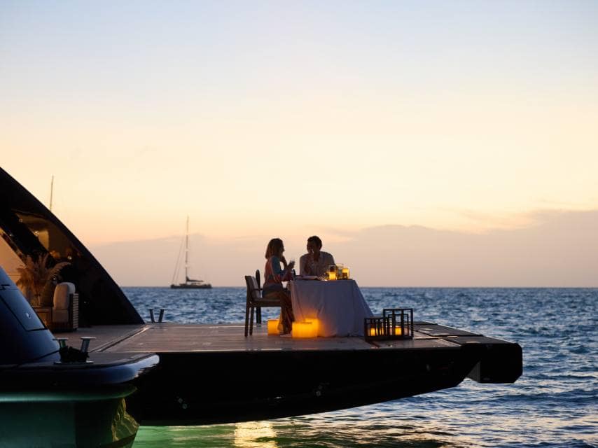 Candlelit dinner aboard a luxury yacht in Santorini, island of myth and volcanic legends.