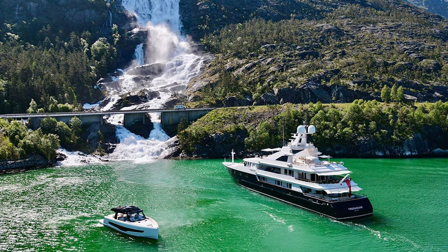 Yachts for charter in a breathtaking fjord, framed by lush greenery and a beautiful waterfall view.