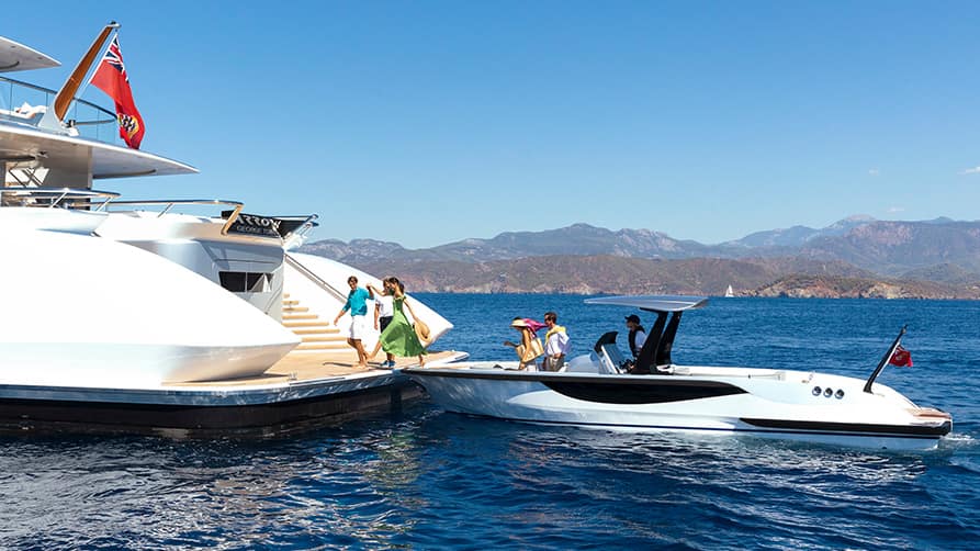 Family boarding their yacht for charter from a speedboat in scenic coastal waters under clear skies.