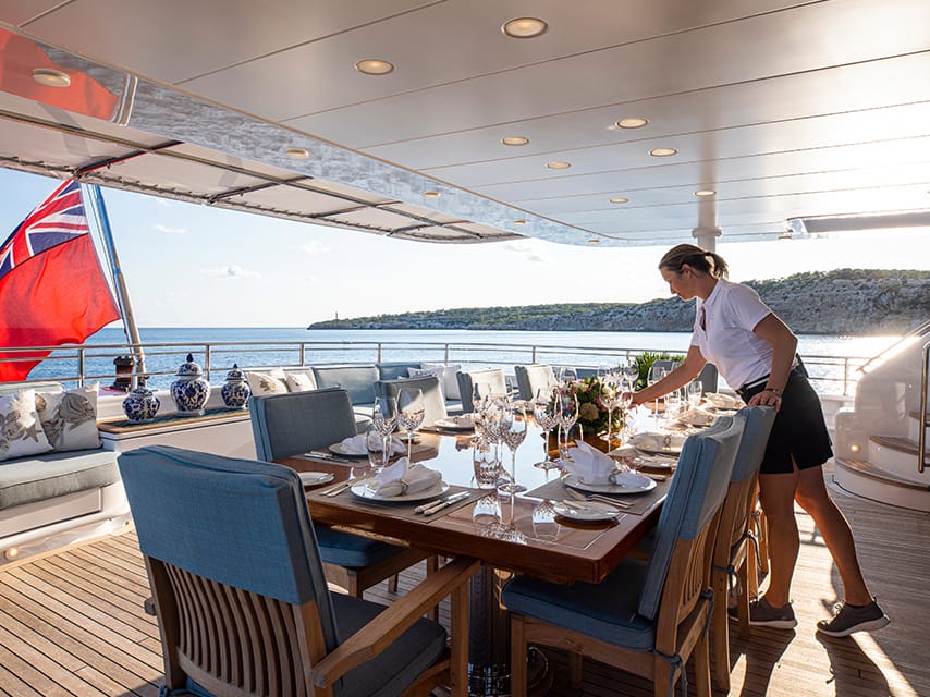 An Edmiston crew member prepares the dinner table for a gourmet sunset dinner during a luxury corporate yacht charter event.