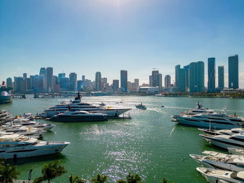 Miami yachts line the coast, ready for visitors to the Miami Boat Show 2026, framed by sun-soaked beaches and modern cityscape views.