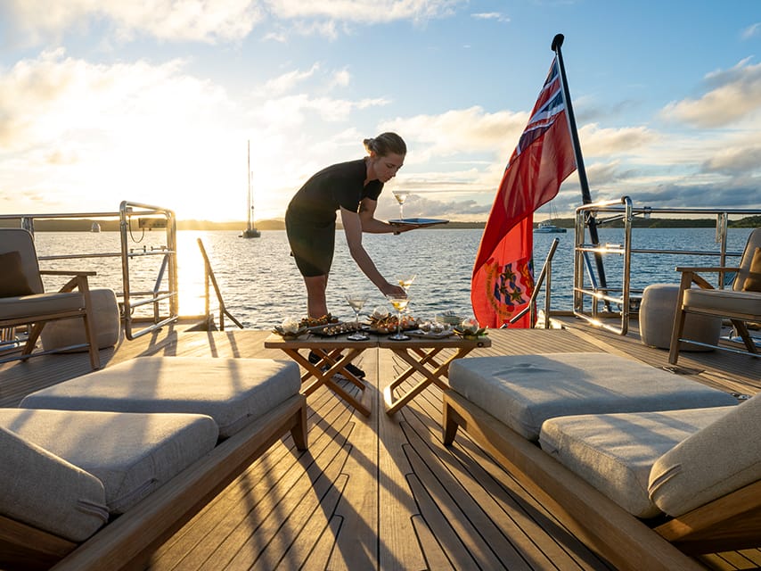 An Edmiston stewardess sets a table on ASAHI, a luxury superyacht charter, St Barths Bucket Regatta's premium viewing spot.
