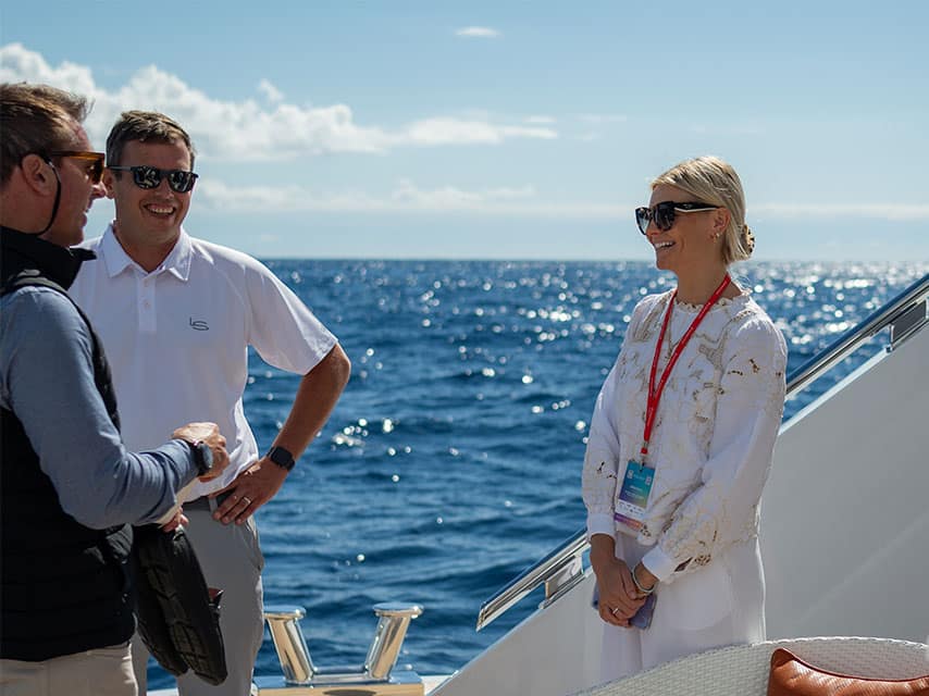 Cultured brokers of the MYBA show and Edmiston engage in a professional discussion on a yacht deck overlooking the blue ocean.