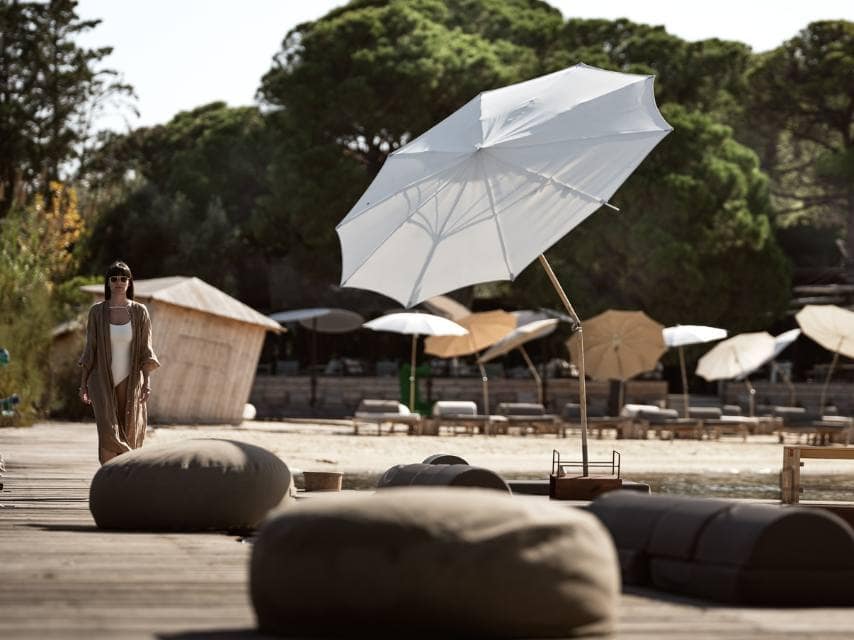 A woman walks among lounge pillows and parasols at Ekies All Senses Resort, a luxury retreat blending nature and boho vibes for your yacht charter in Greece.
