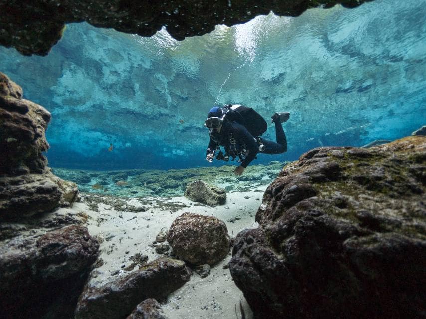 A scuba diver enters a submerged cave beneath Mediterranean towering cliffs during a Sardinia yacht charter.