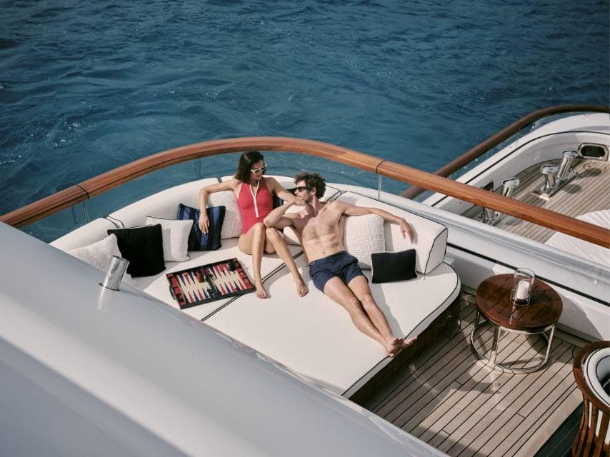 Couple lounges on SOPHIA sundeck, soaking up views on their luxury yacht honeymoon.
