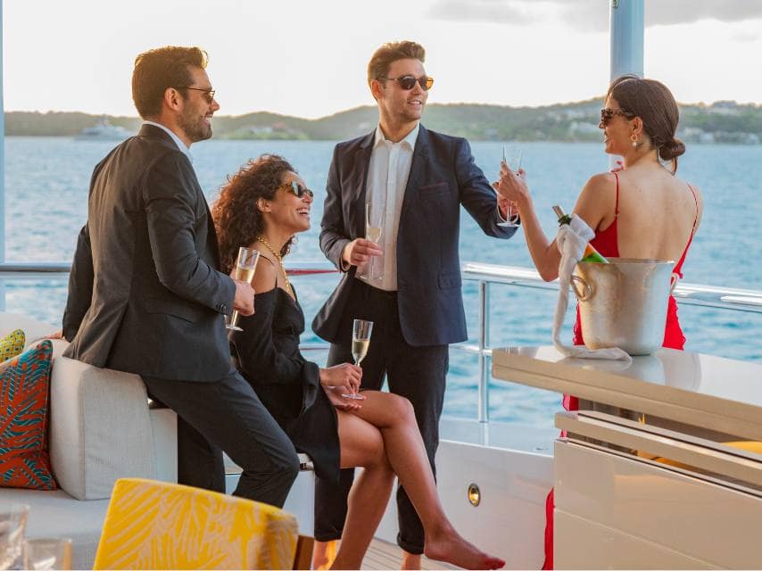 Friends laugh over sunset cocktails during a private yacht wedding at sea.