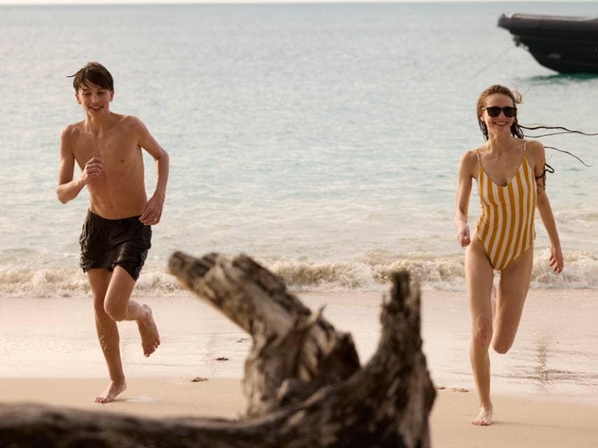Kids playing in the sand near a superyacht during a cinematic-style treasure hunt on a med yacht charter.