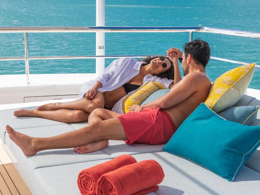 A couple laughs together on the deck, enjoying a private moment with the sea as their backdrop during their luxury yacht honeymoon.