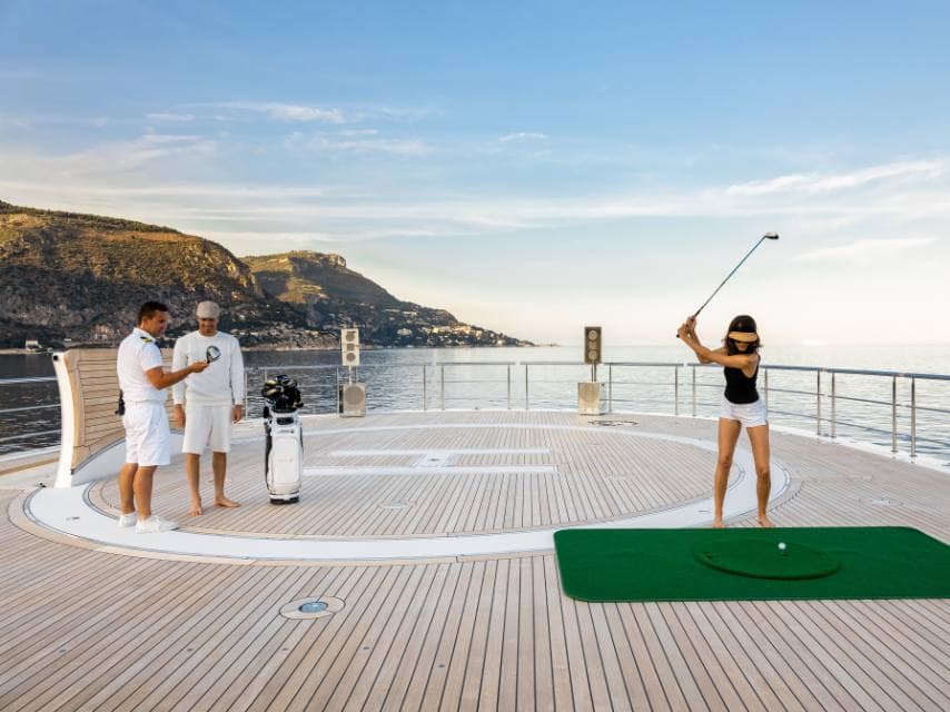 Swing practice on board: golf setup on the sundeck of a wellness-focused yacht retreat.