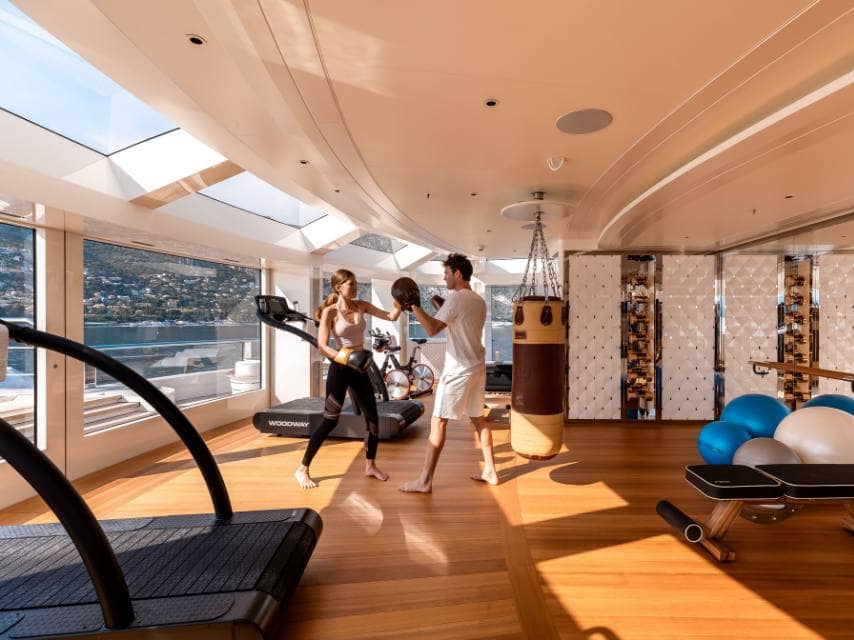 Yacht personal trainer leads a wellness session in the gym aboard a luxury yacht charter, offering tailored fitness at sea.