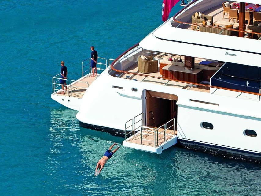 A man dives from his superyacht into clear waters at Voutoumi Beach, Antipaxos, Greece, a tranquil Ionian stop for a luxury yacht charter