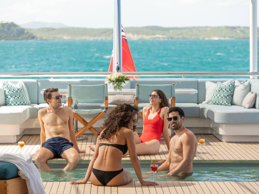 Friends relax in the pool aboard a caribbean superyacht charter in paradise waters.