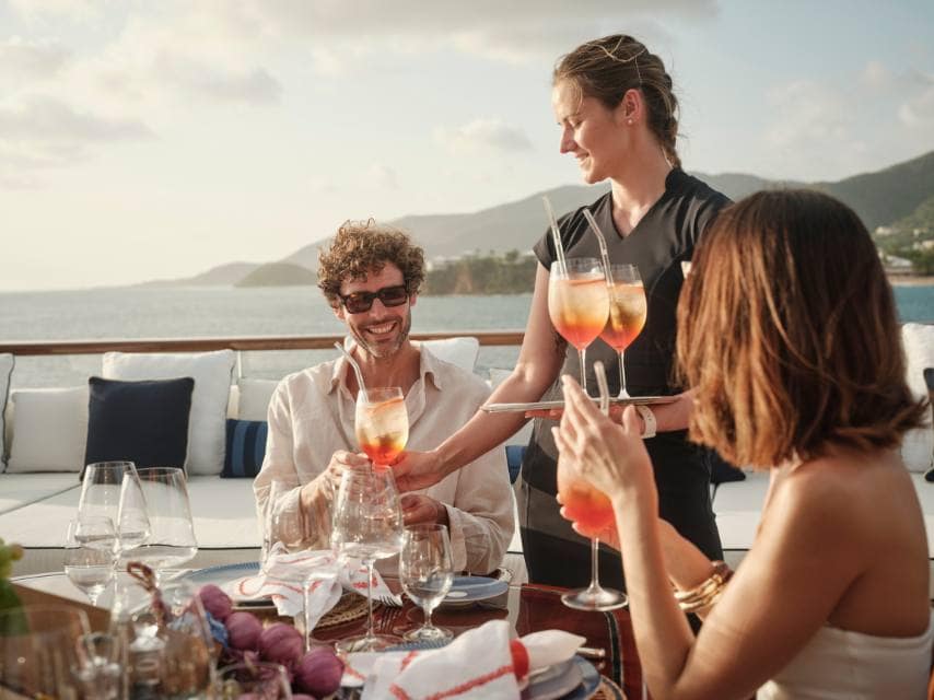 A yacht Christmas party in the Caribbean comes alive as crew members serve festive drinks on board.
