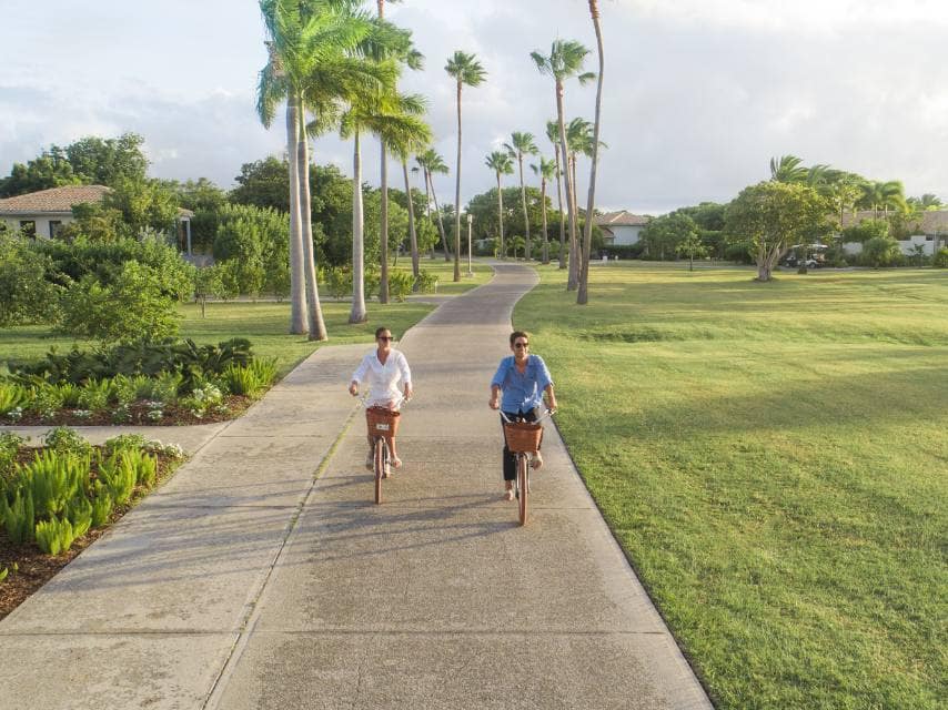 A couple cycles along palm-lined island paths at Jumby Bay during their Caribbean superyacht charter experience.