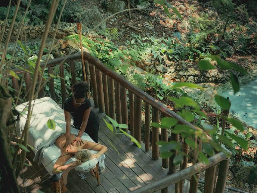 A woman enjoys spa retreat Caribbean luxury with a massage in the lush Eden Roc forest.