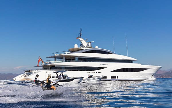 A couple on jet skis with their luxury yacht charter in the background