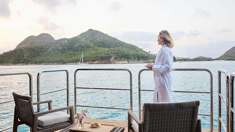 A woman enjoying coffee while taking in the view of the colorful islands on her private Galapagos yacht charter.