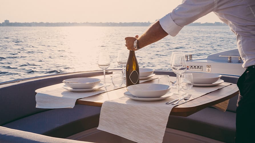 A server places a beautiful bottle of white yacht wine on a dinner table, set against a stunning ocean view.