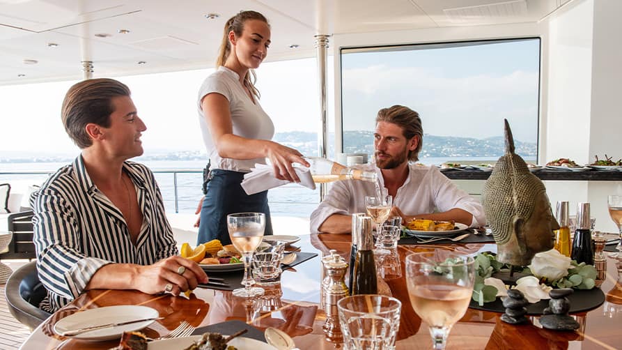 Two men enjoying dinner and a glass of wine from their private yacht wine cellar.