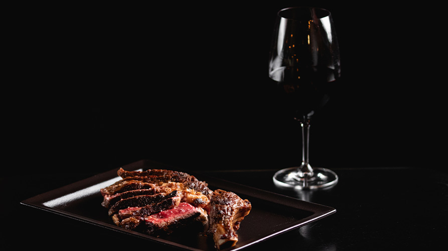 A plate of thinly sliced steak and a glass of red wine fade into the dark background at Dans Le Noir in Marseille, where French Riviera cuisine is served as a gourmet meal in complete darkness.