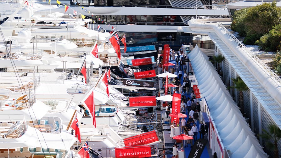 A stunning array of Edmiston yachts is parked at the dock at the Monaco Yacht Show 2024, as a crowd of people passes by.