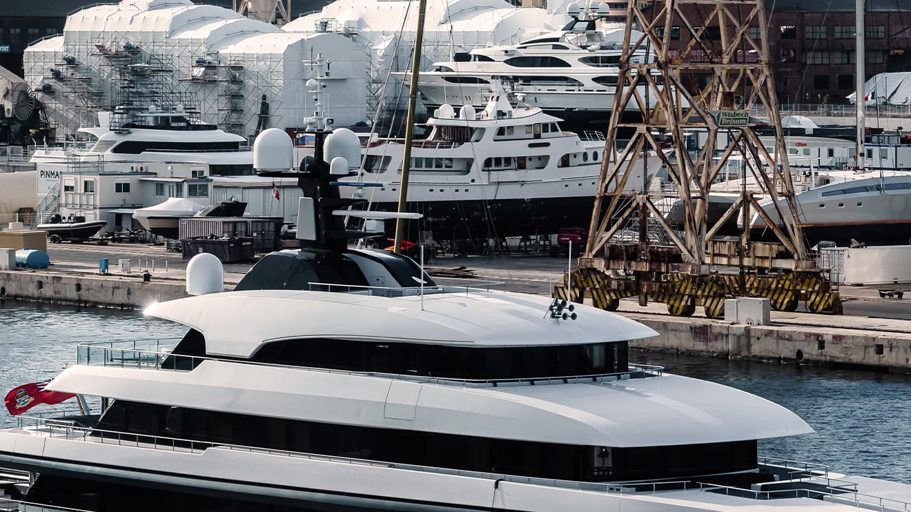 Large superyacht with a yacht building shipyard in the background