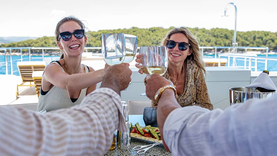 Friends make a toast to the beautiful selection of yacht wines available on their superyacht charter.