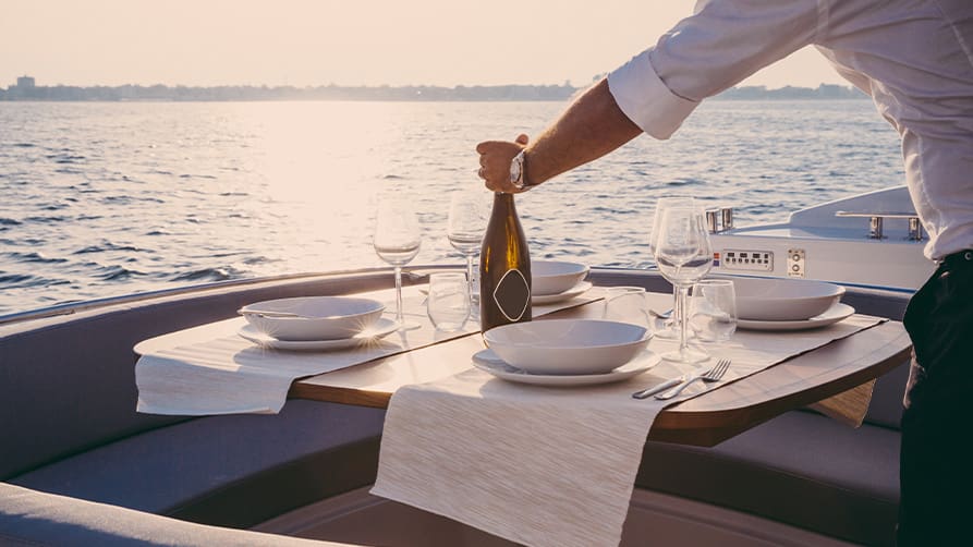A server places a beautiful bottle of white yacht wine on a dinner table, set against a stunning ocean view.