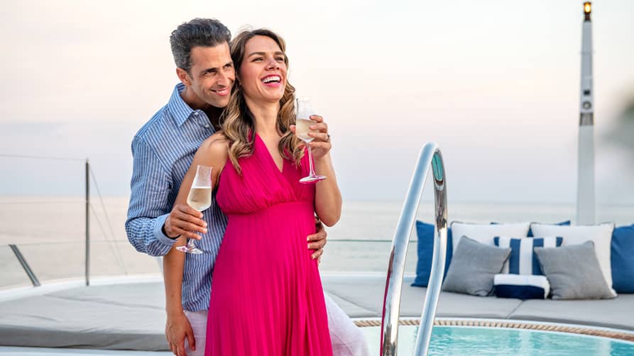 A smiling couple enjoying a glass of their yacht wine on deck.