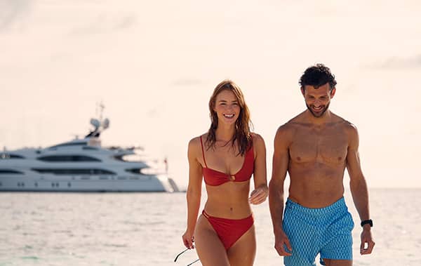 A couple on a beach with their luxury yacht charter in the background